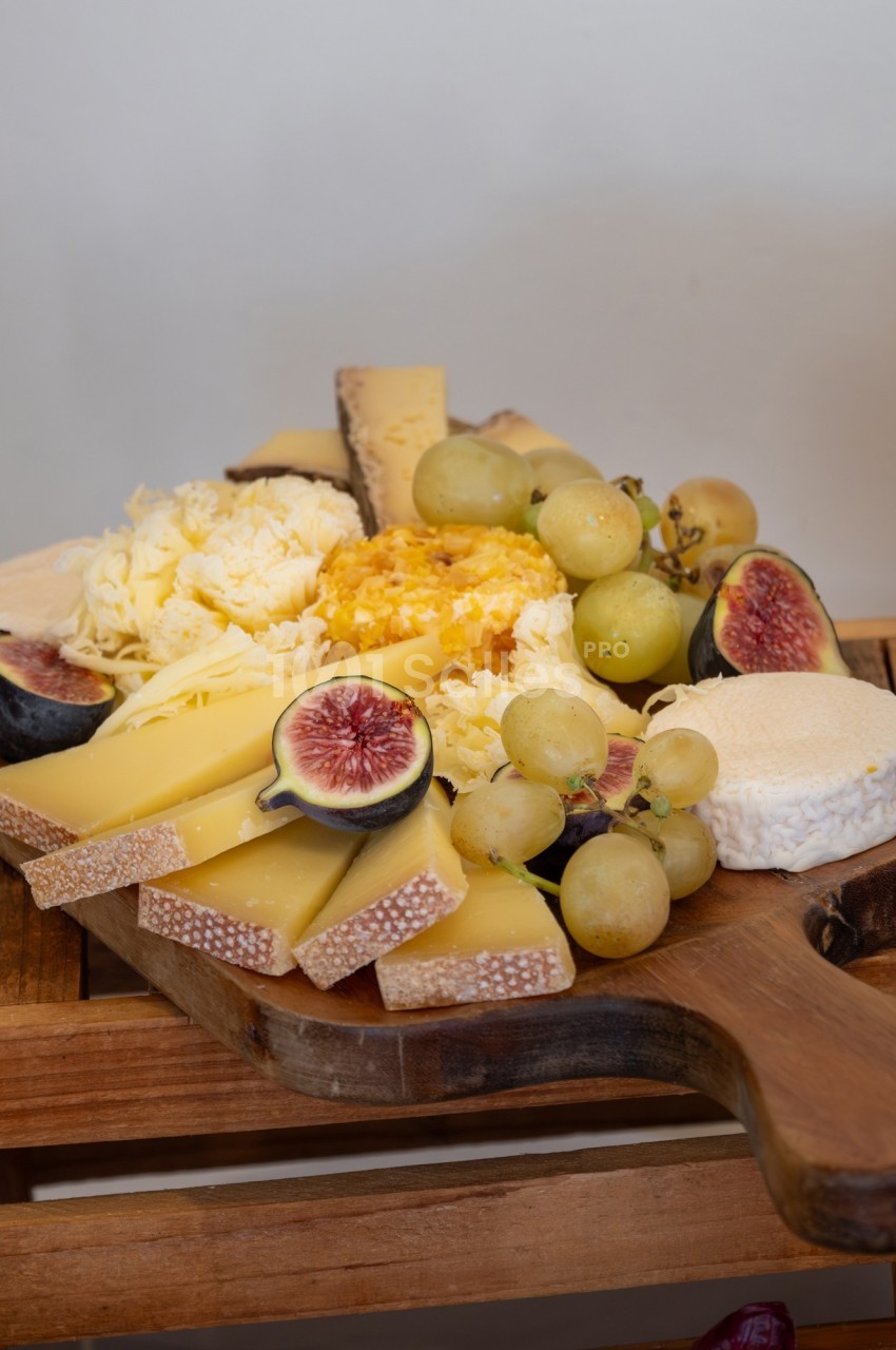 Plateau de fromages variés avec raisins, figues et miel, présenté sur une planche en bois.