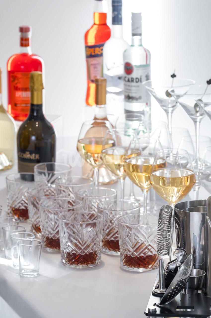 Verres de cocktails remplis et bouteilles d'alcool variées disposés sur une table blanche.