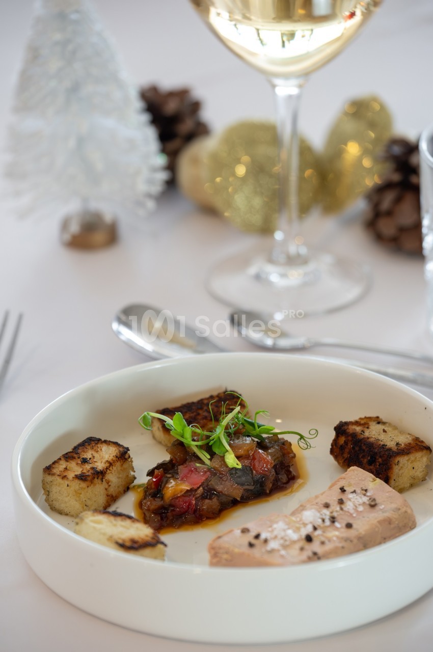 Assiette gastronomique avec foie gras, croûtons dorés et garniture, décor festif en arrière-plan.