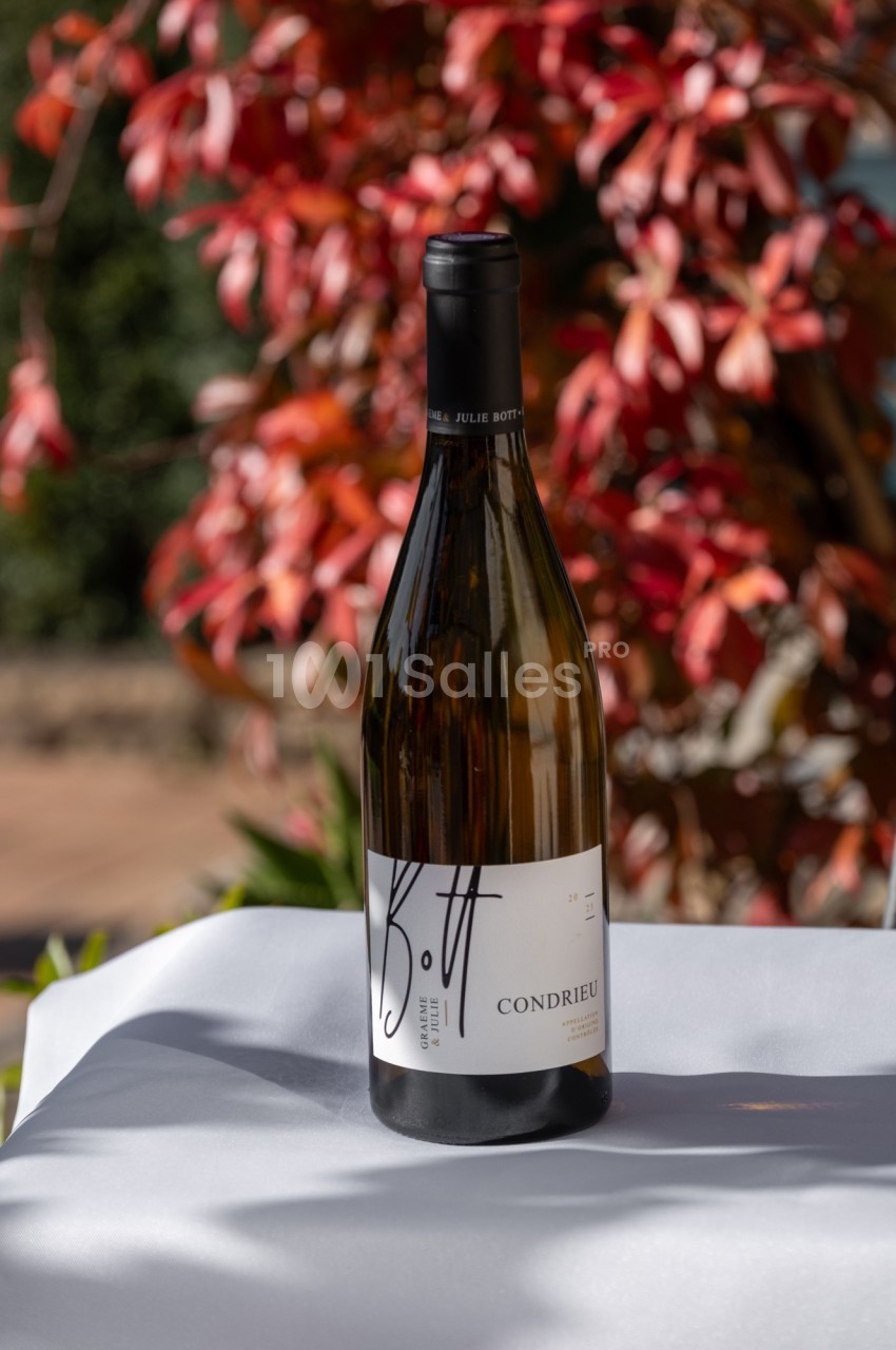 Bouteille de vin blanc Condrieu posée sur une table blanche, avec un arrière-plan de feuillage rouge et vert.