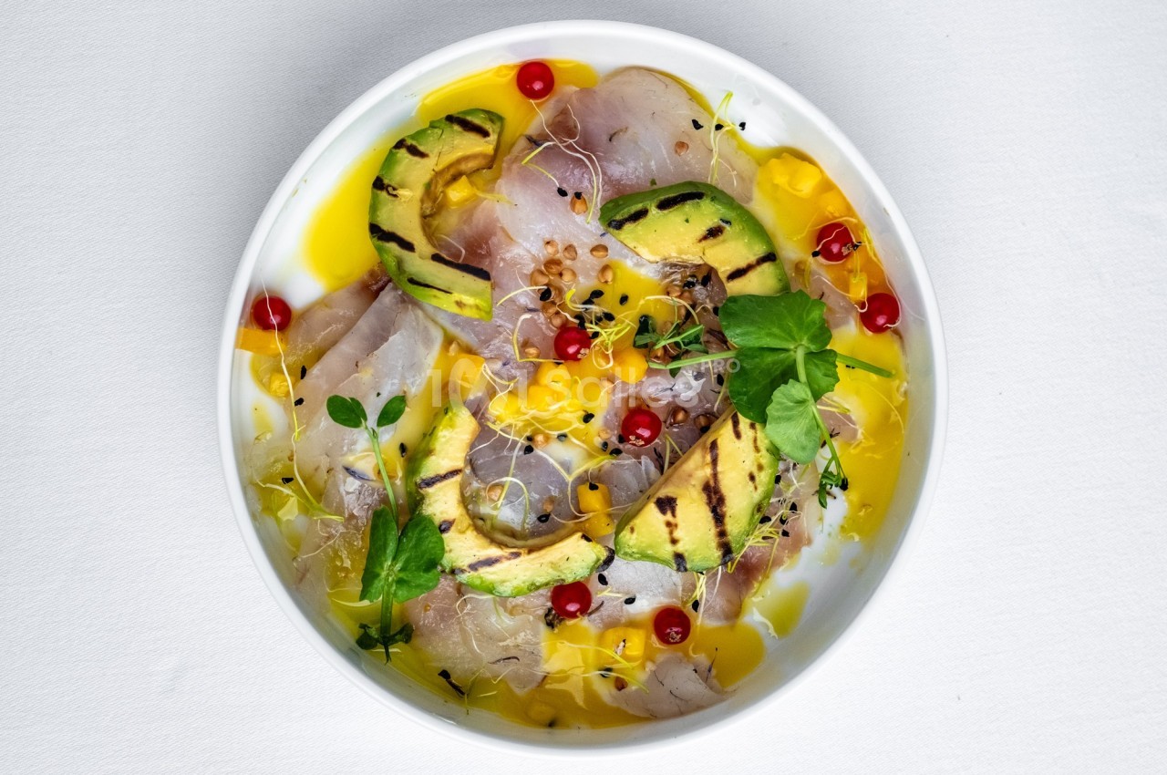 Assiette de carpaccio de poisson cru avec avocat grillé, groseilles rouges, pousses et sauce jaune.