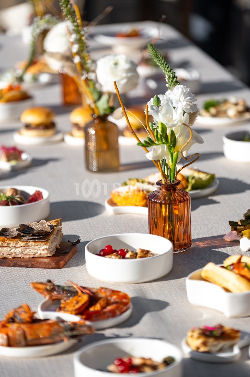Table dressée avec des plats variés, incluant fruits de mer, tartines et desserts, décorée de fleurs blanches en vase.