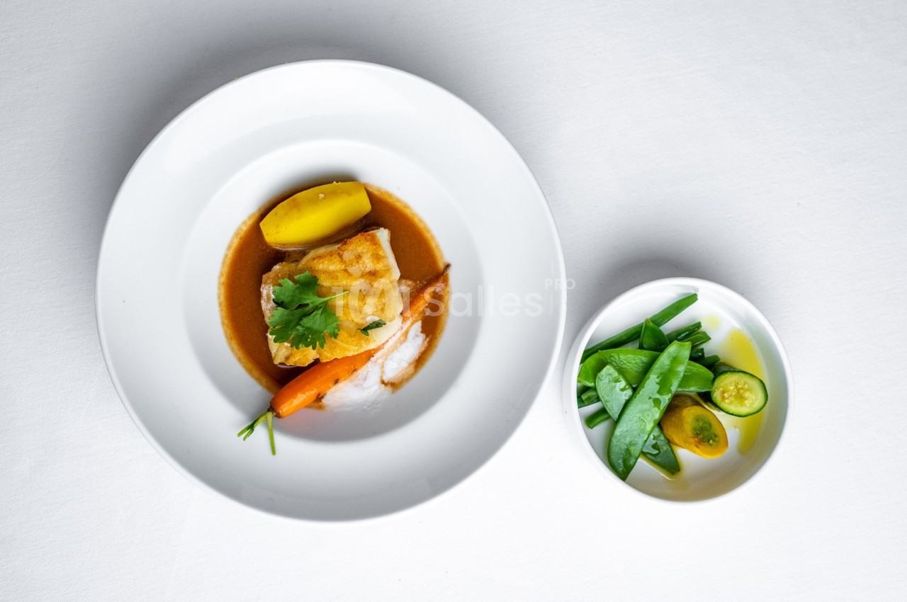 Assiette de poisson accompagné de légumes et sauce, avec un bol de pois gourmands et tomates en garniture.