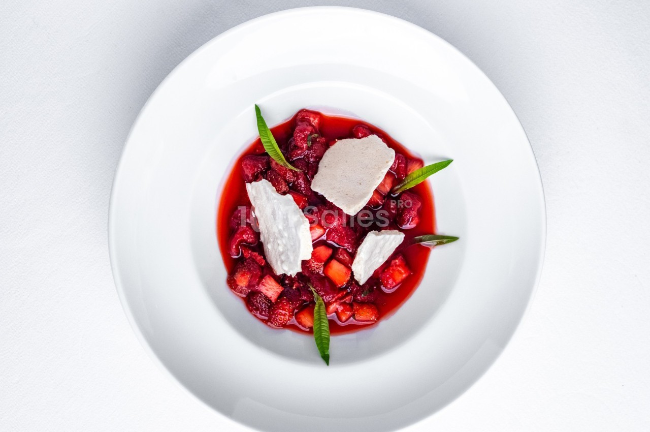 Dessert composé de fruits rouges, morceaux de meringue et feuilles décoratives, présenté dans une assiette blanche.