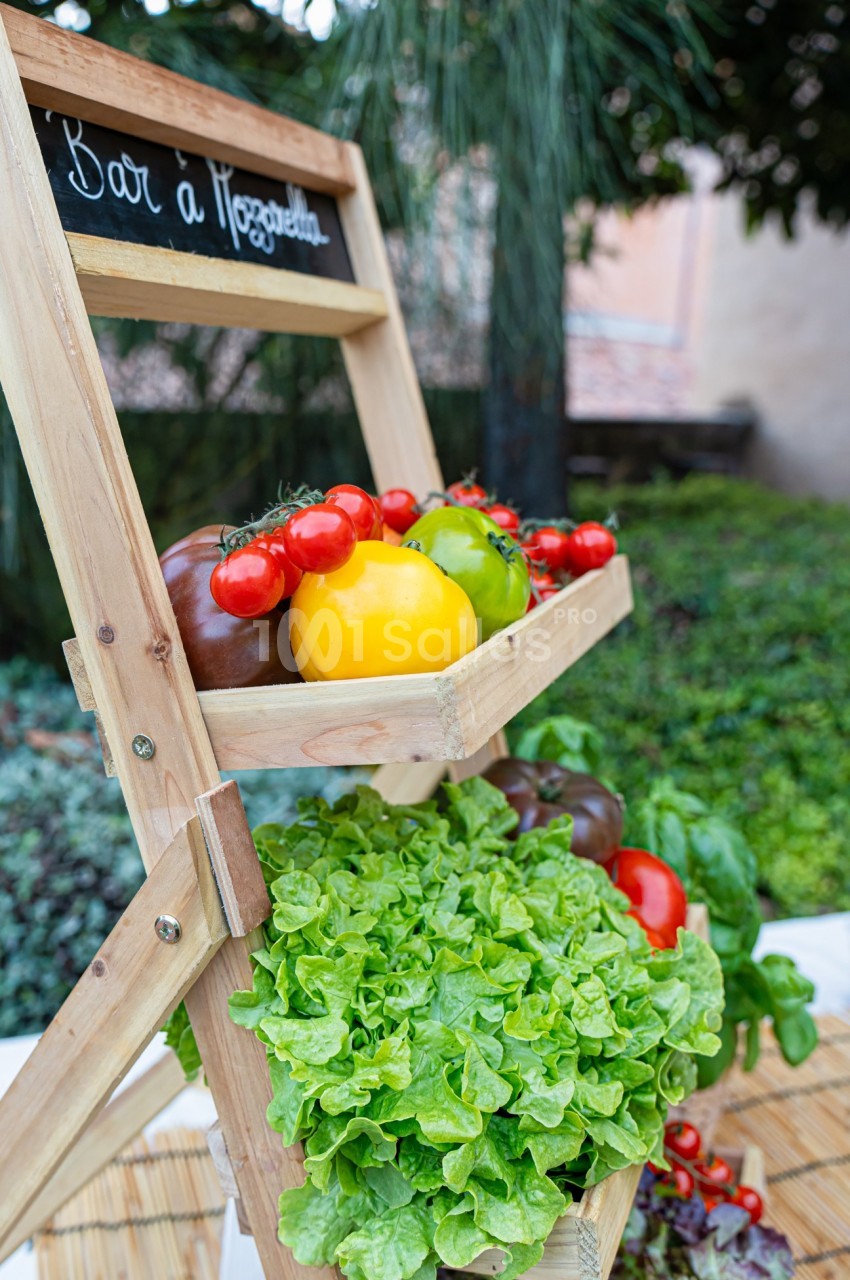 Présentoir en bois avec des légumes frais, dont tomates, poivrons et laitue, disposé en extérieur près de végétation.