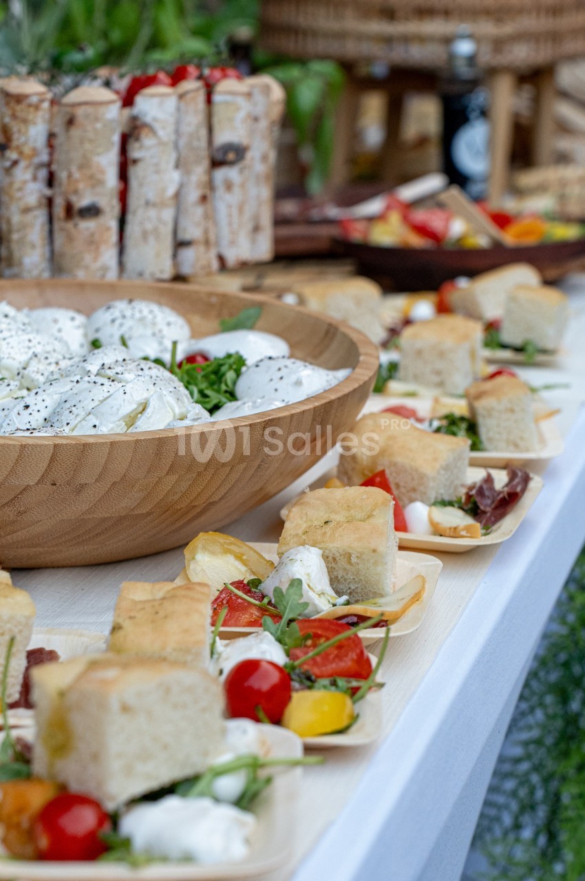 Buffet avec salade de mozzarella, légumes frais, focaccia et divers plats disposés sur une table blanche.