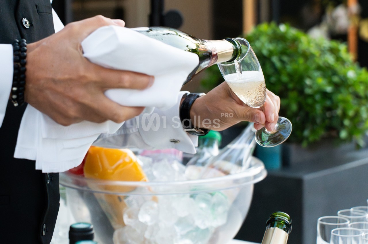 Un serveur verse du champagne dans une flûte près d'un seau rempli de glace et de bouteilles.