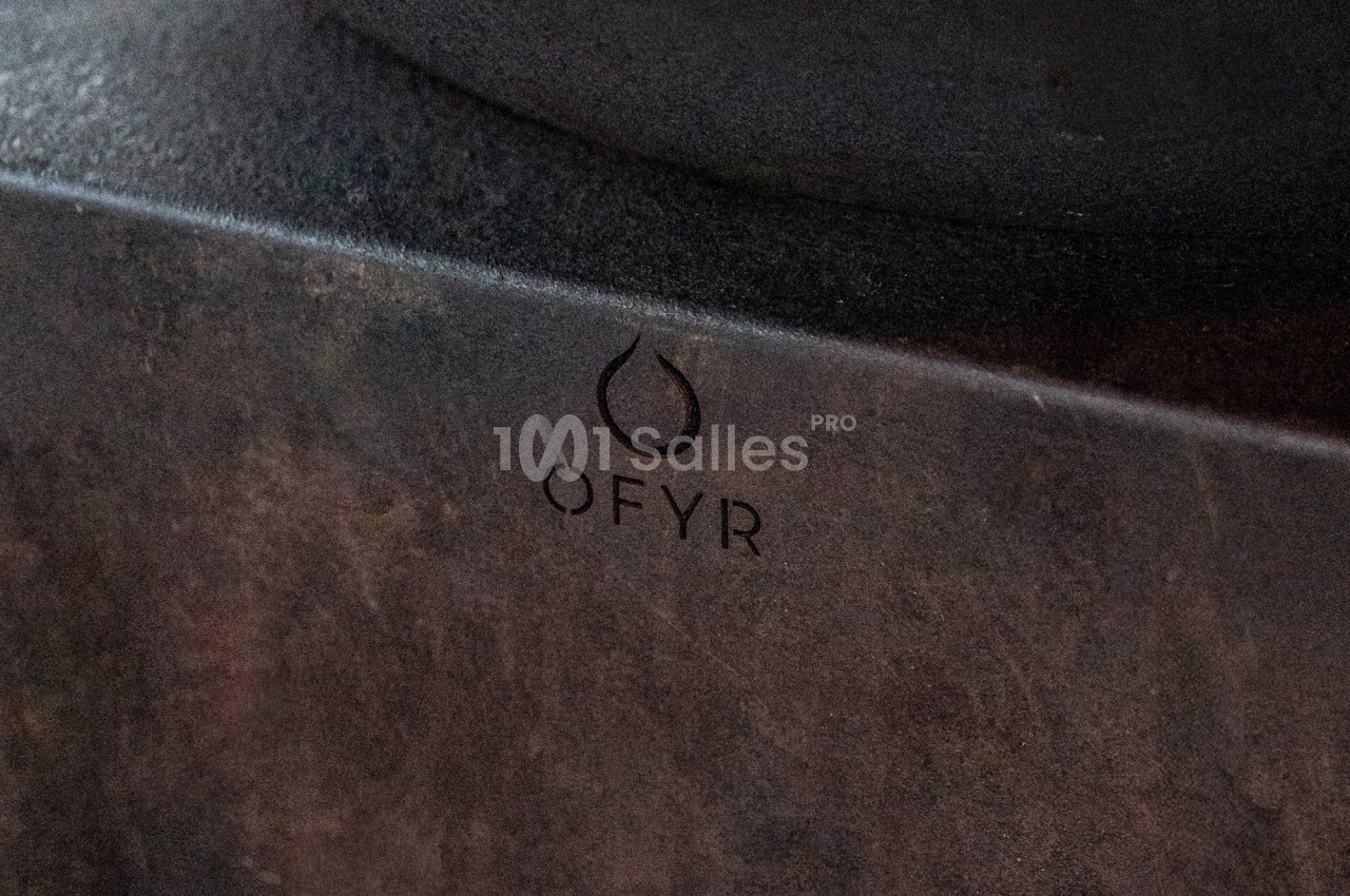 Logo ’OFYR’ gravé sur une surface métallique sombre et texturée.