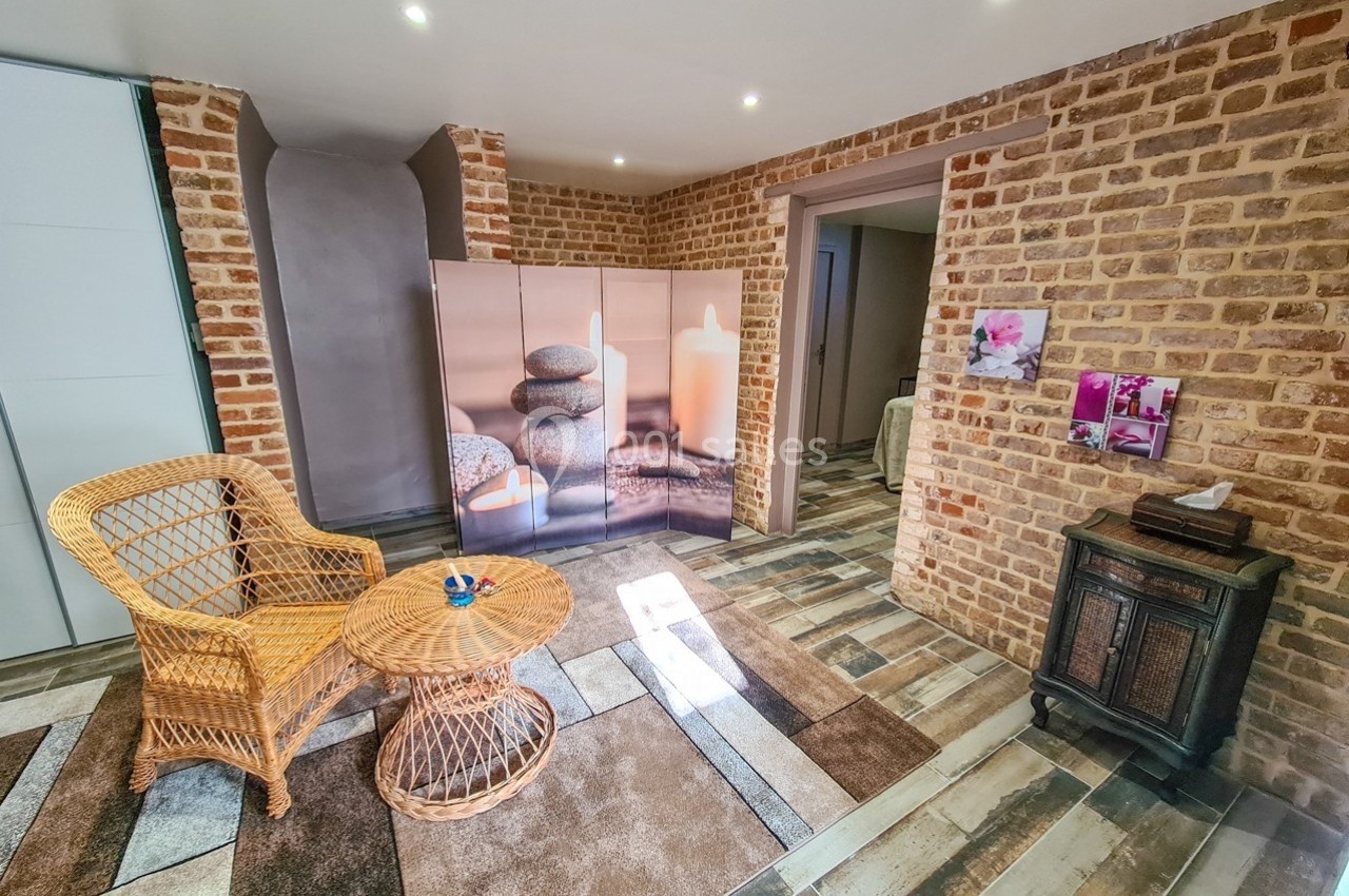 Espace intérieur avec mur en briques, fauteuil et table en rotin, paravent décoratif et sol en carreaux modernes.