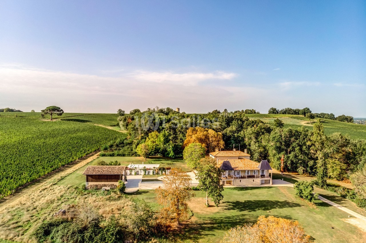 Vue aérienne d'une maison entourée de champs, d'arbres et d'un espace extérieur aménagé avec piscine.