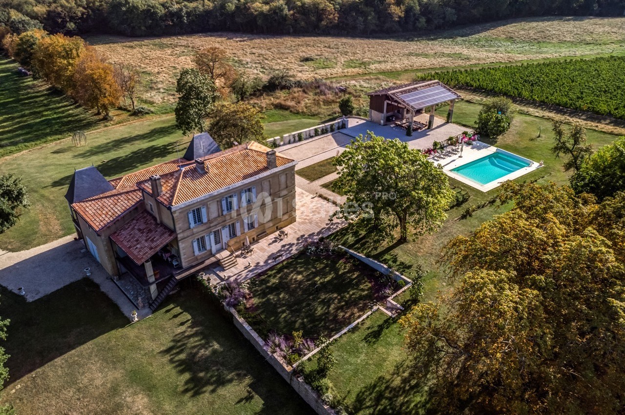 Vue aérienne d'une maison en pierre avec piscine, terrasse et jardin, entourée de champs et d'arbres.