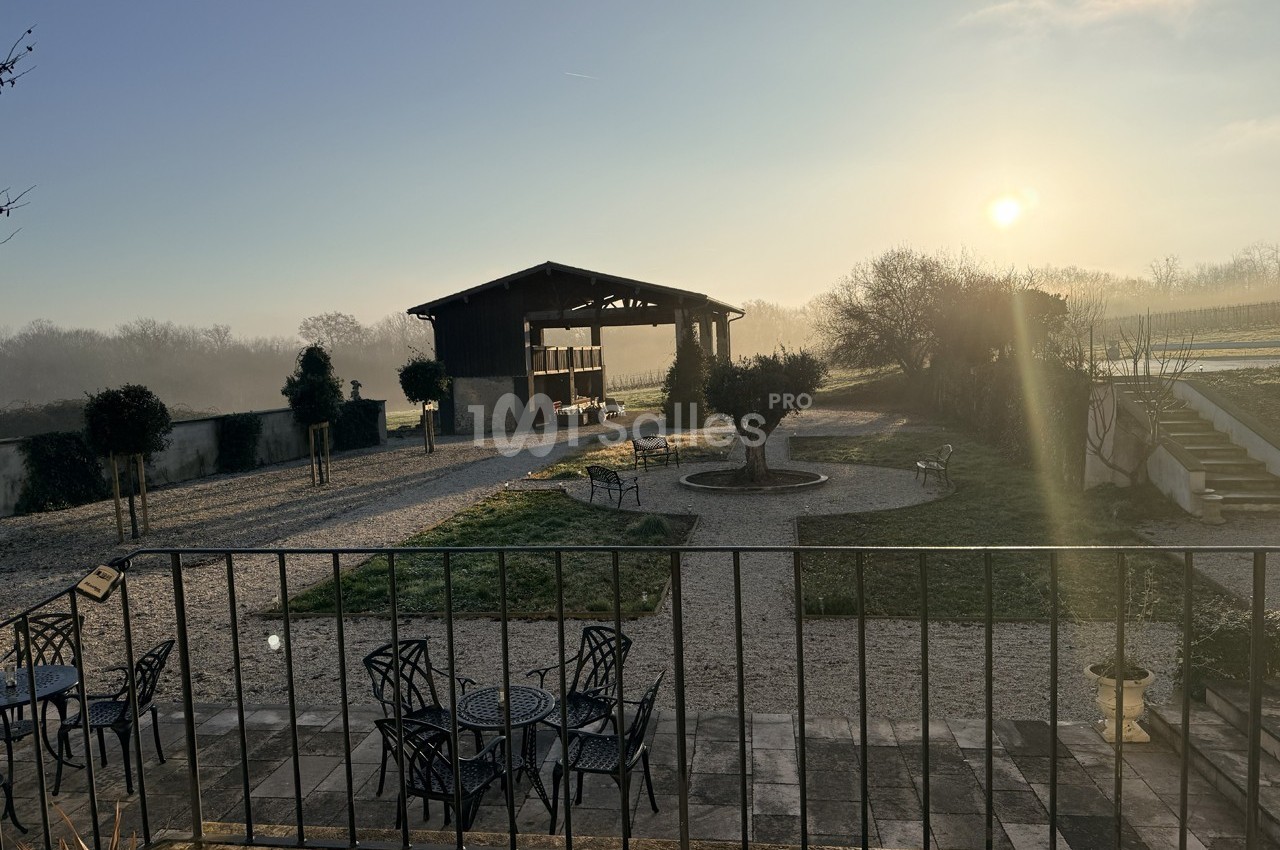 Cour extérieure avec mobilier de jardin, vue sur un bâtiment ouvert et un paysage rural au lever du soleil.