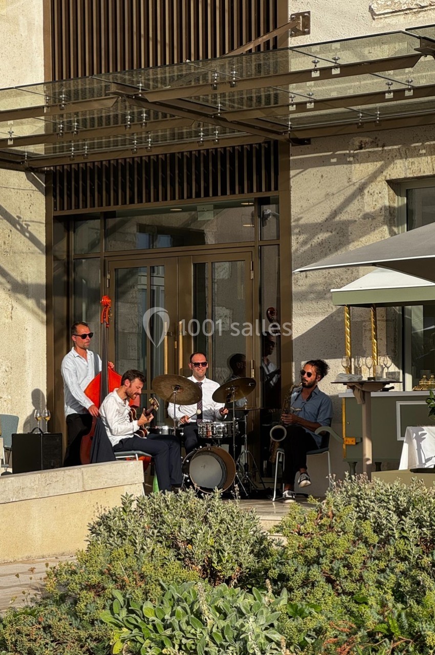 Un groupe de musiciens joue en plein air devant un bâtiment moderne, entouré de végétation.
