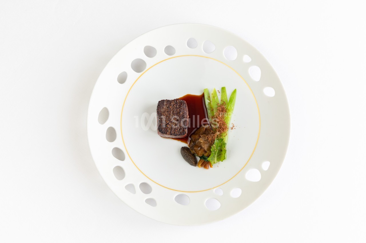 Assiette gastronomique avec un morceau de viande, sauce, légumes verts et morilles, présentée sur un fond blanc.
