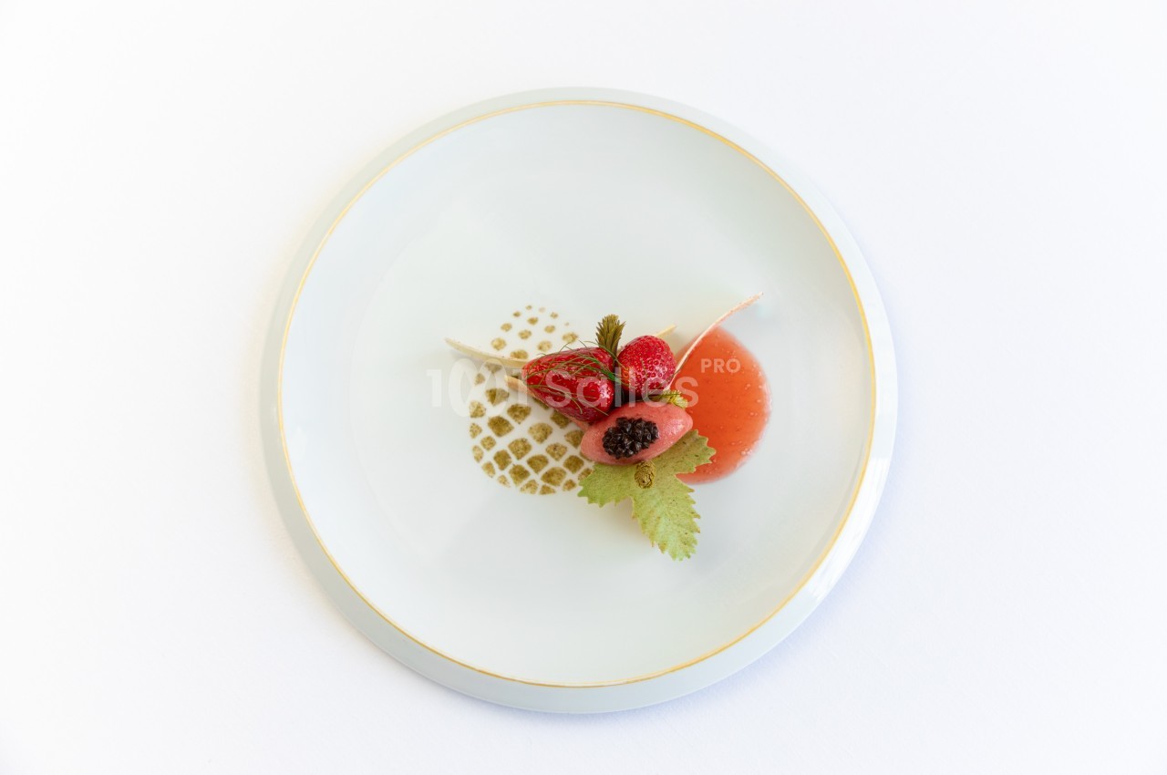 Assiette blanche avec un dessert raffiné composé de fraises, d'une sauce rouge et de décorations artistiques.