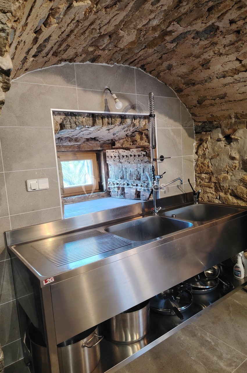Évier en inox avec robinet flexible, installé dans une cuisine en pierre avec une ouverture donnant sur l'extérieur.