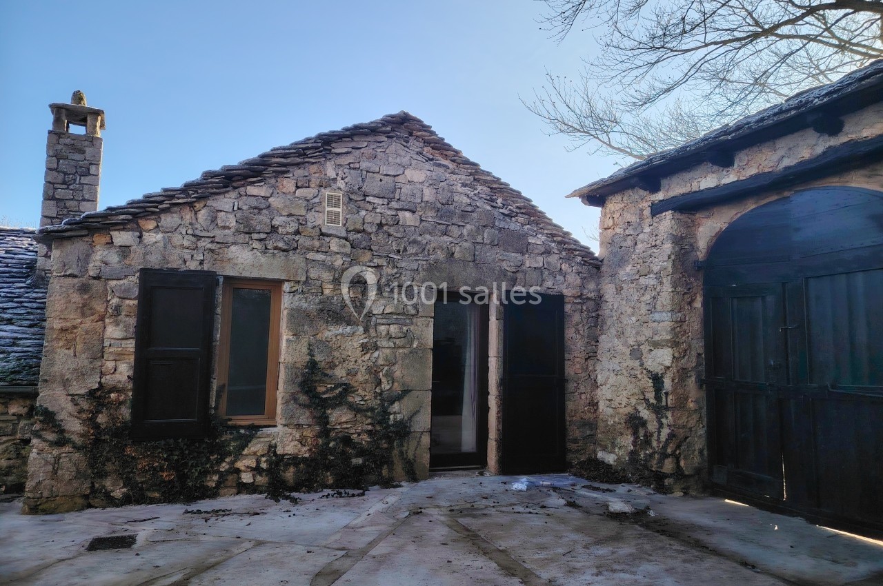 Maison en pierre traditionnelle avec toit en lauze, entourée d'une cour pavée et d'arbres dénudés en hiver.