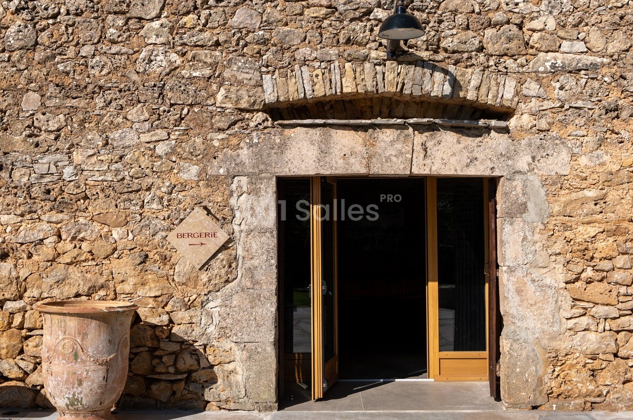 Entrée d'une bergerie en pierre avec une porte en bois ouverte et un pot en terre cuite à gauche.