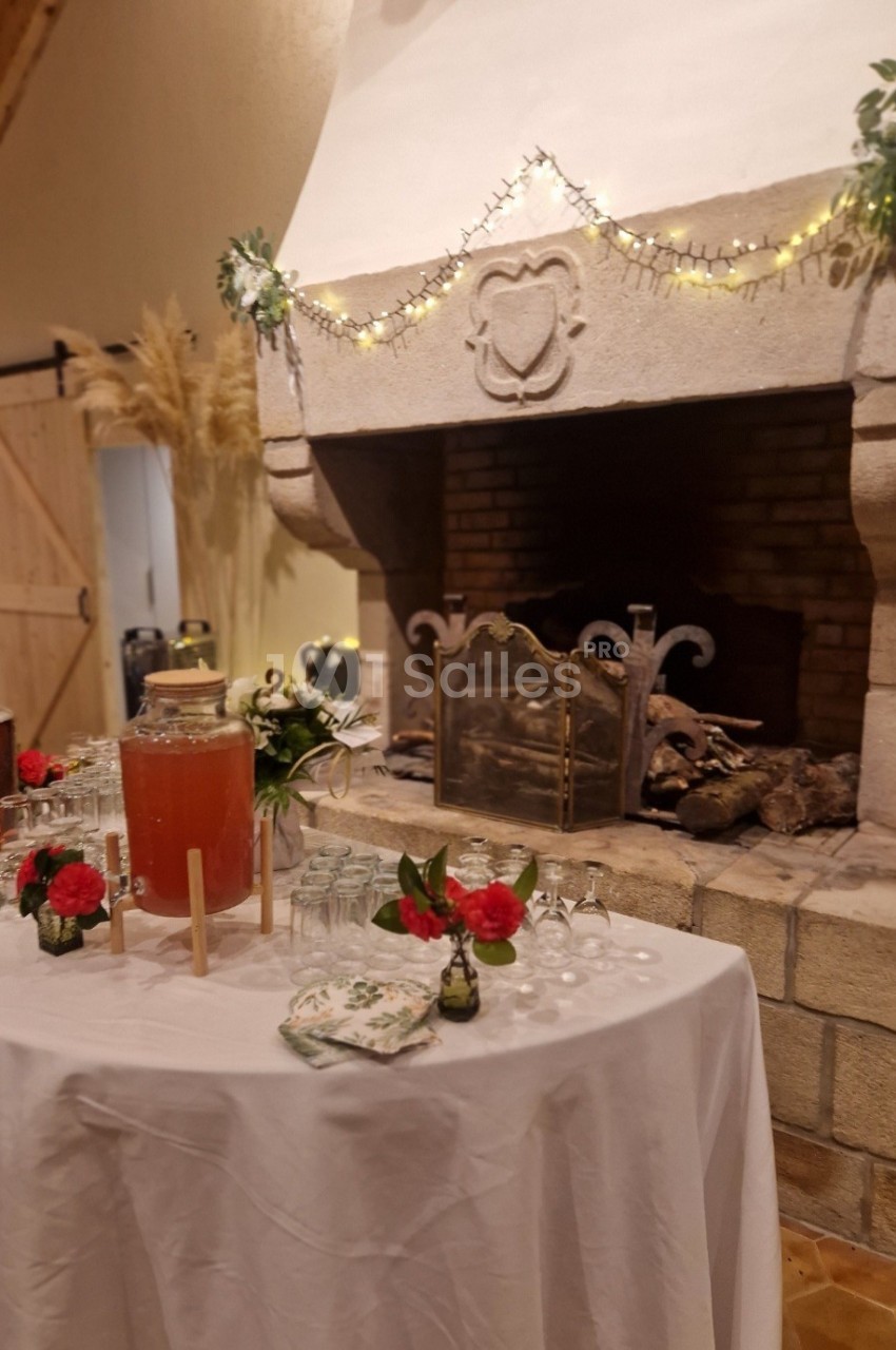 Table décorée avec boissons et fleurs devant une cheminée en pierre ornée de guirlandes lumineuses.