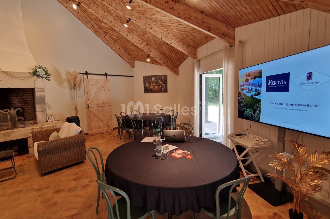 Salle de réunion avec tables rondes, cheminée, écran affichant une présentation et décoration intérieure chaleureuse.