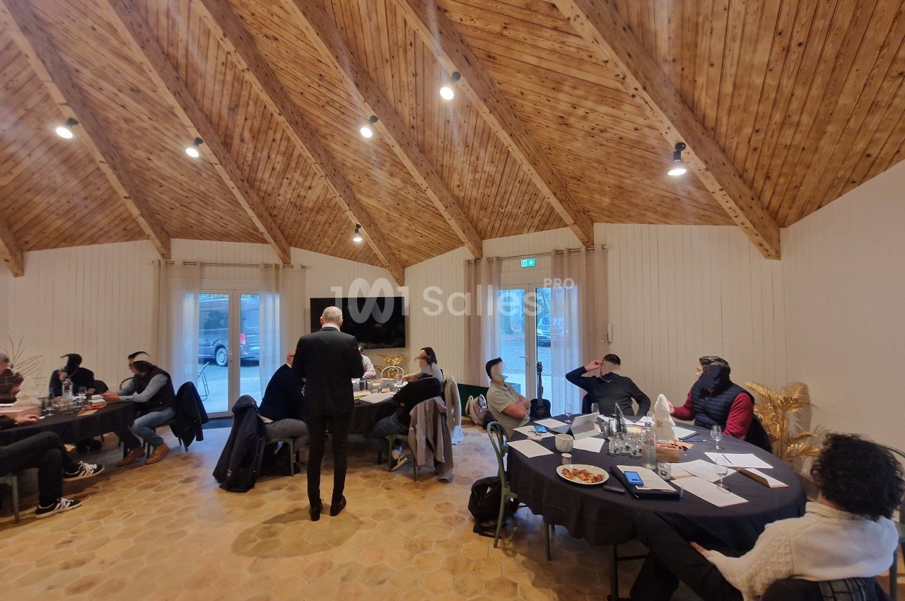 Personnes assises autour de tables dans une salle avec plafond en bois, participant à une réunion ou un atelier.