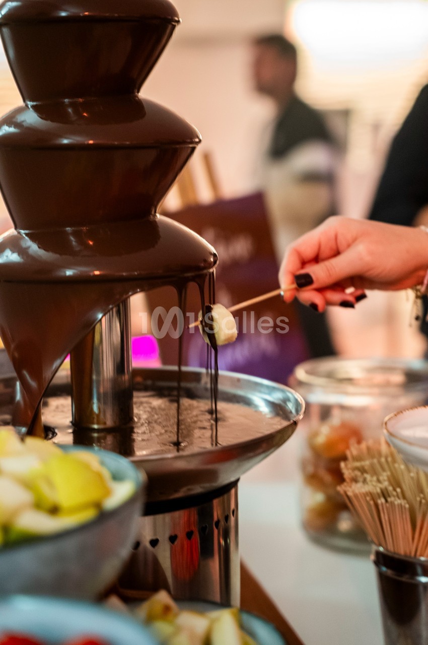 Fontaine de chocolat avec une personne trempant un morceau de fruit sur une brochette.
