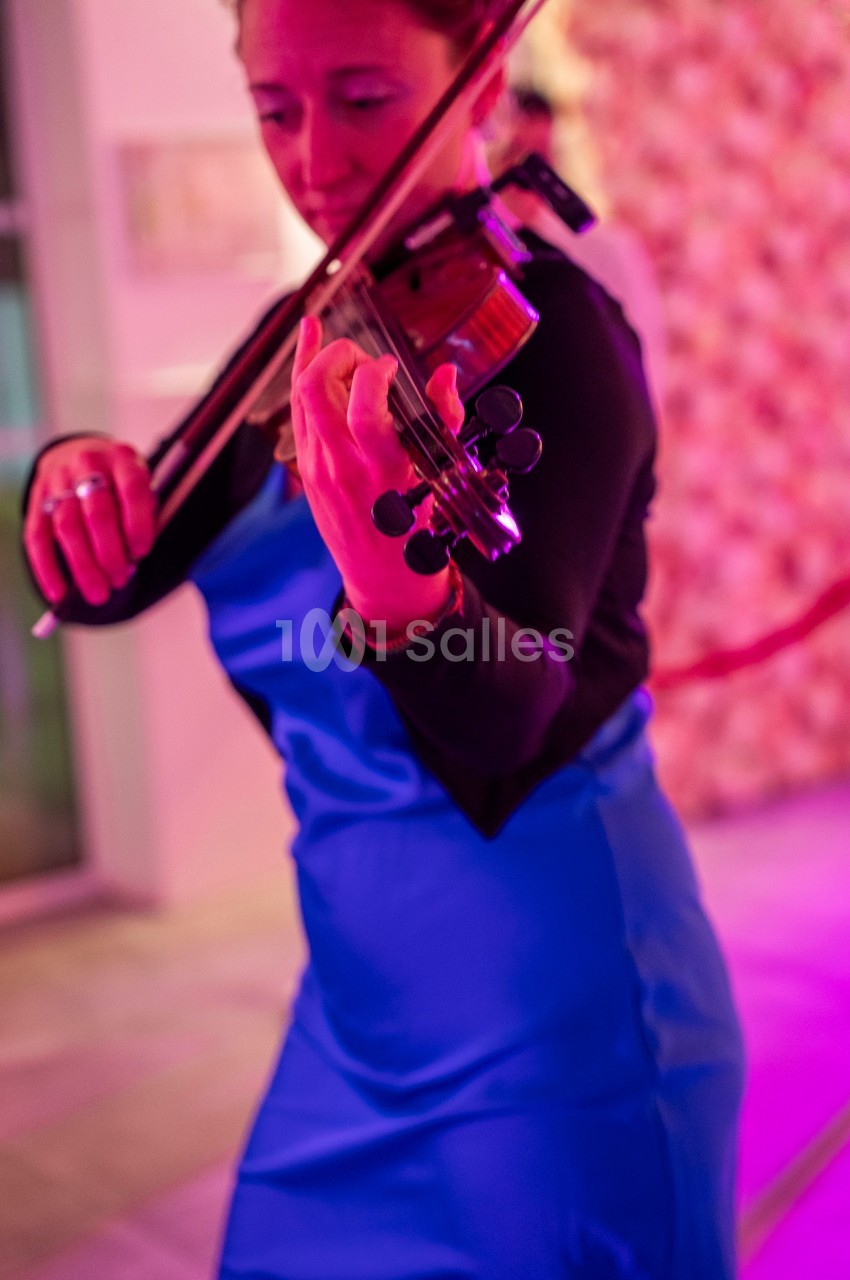 Une femme en robe bleue joue du violon dans un environnement éclairé par des lumières roses.