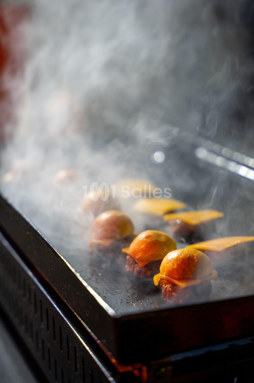 Mini-burgers en train de cuire sur une plaque chauffante, entourés de vapeur.