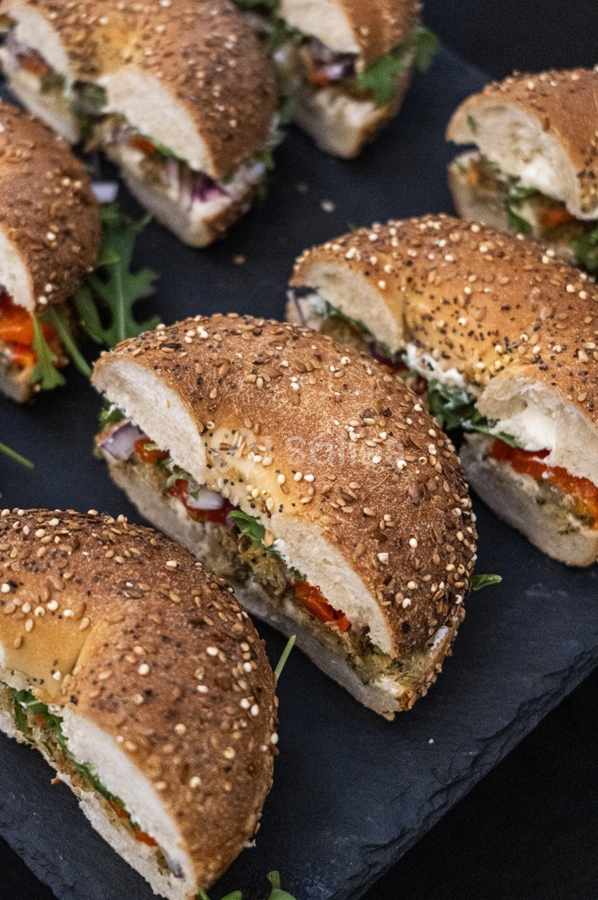 Sandwiches au pain aux graines garnis de légumes frais et de verdure, disposés sur un plateau noir.