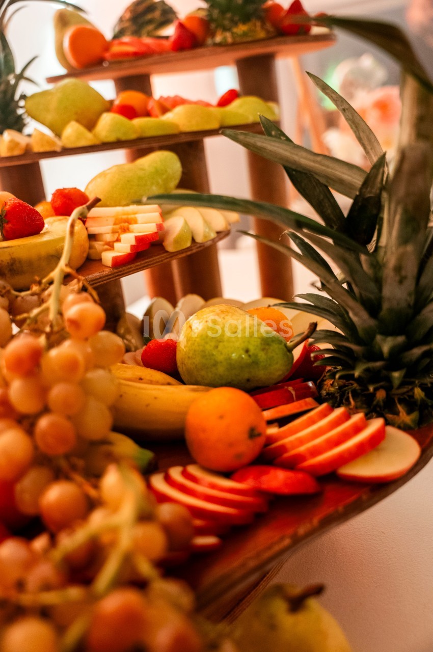 Plateau de fruits variés avec ananas, raisins, pommes tranchées, poires, bananes et agrumes disposés sur plusieurs niveaux.