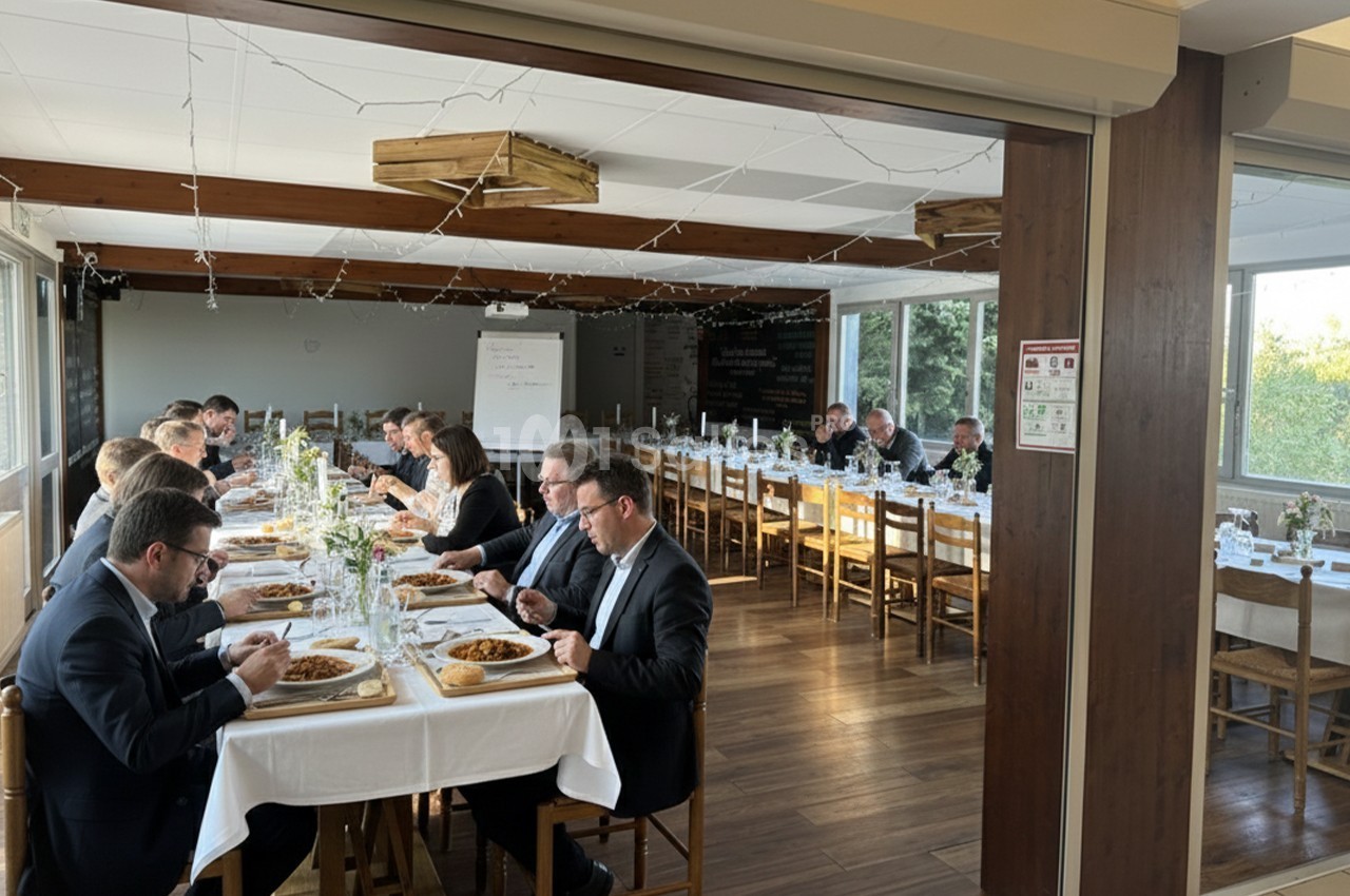 Des personnes en tenue formelle dînent autour de longues tables dans une salle lumineuse avec des décorations simples.