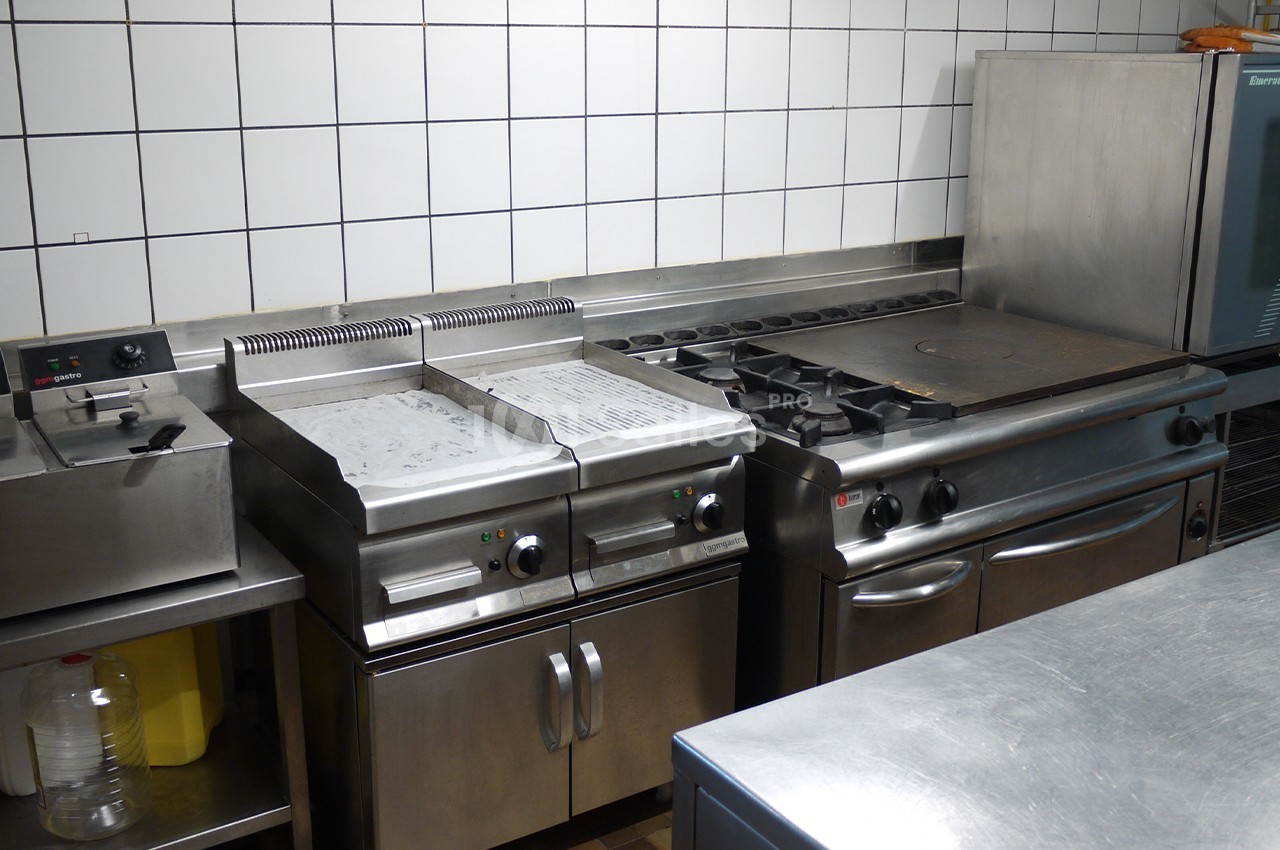 Cuisine professionnelle avec plaques de cuisson, friteuses et four, entourée de surfaces en acier inoxydable.