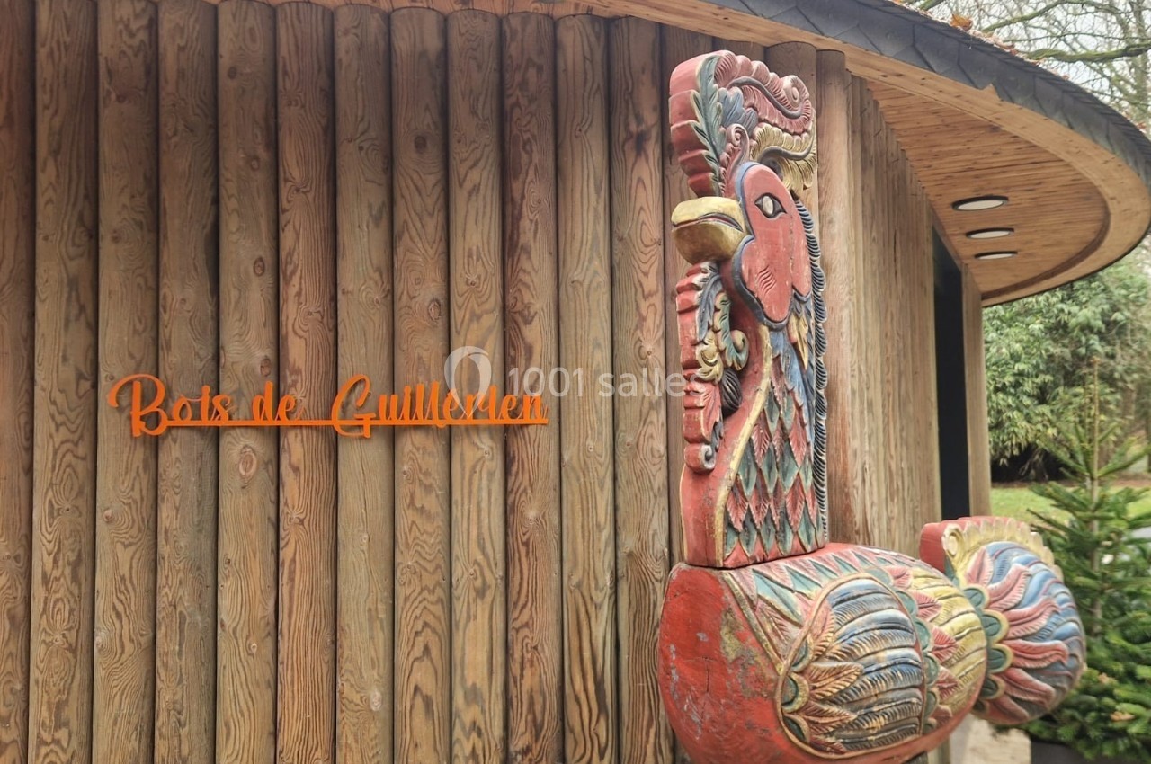 Sculpture colorée en forme d'oiseau devant un bâtiment en bois avec l'inscription ’Bois des Guillemins’.