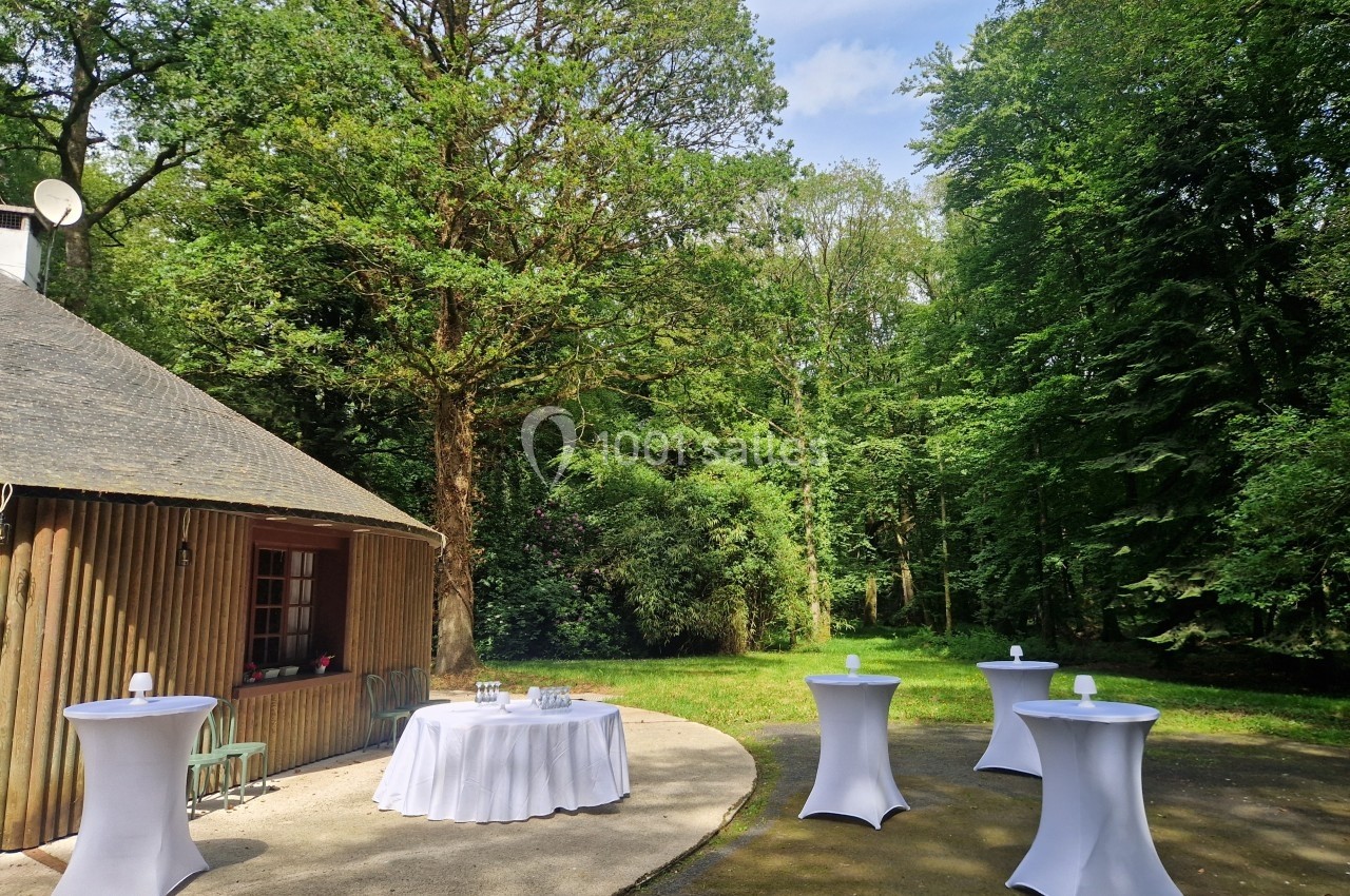 Espace extérieur avec tables hautes dressées et une cabane en bois, entouré d'arbres dans un cadre naturel.