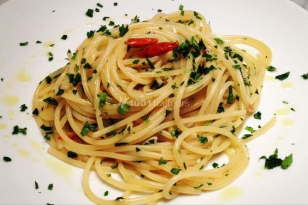 Assiette de spaghetti assaisonnés à l'huile d'olive, piment et persil, présentés sur une table blanche.