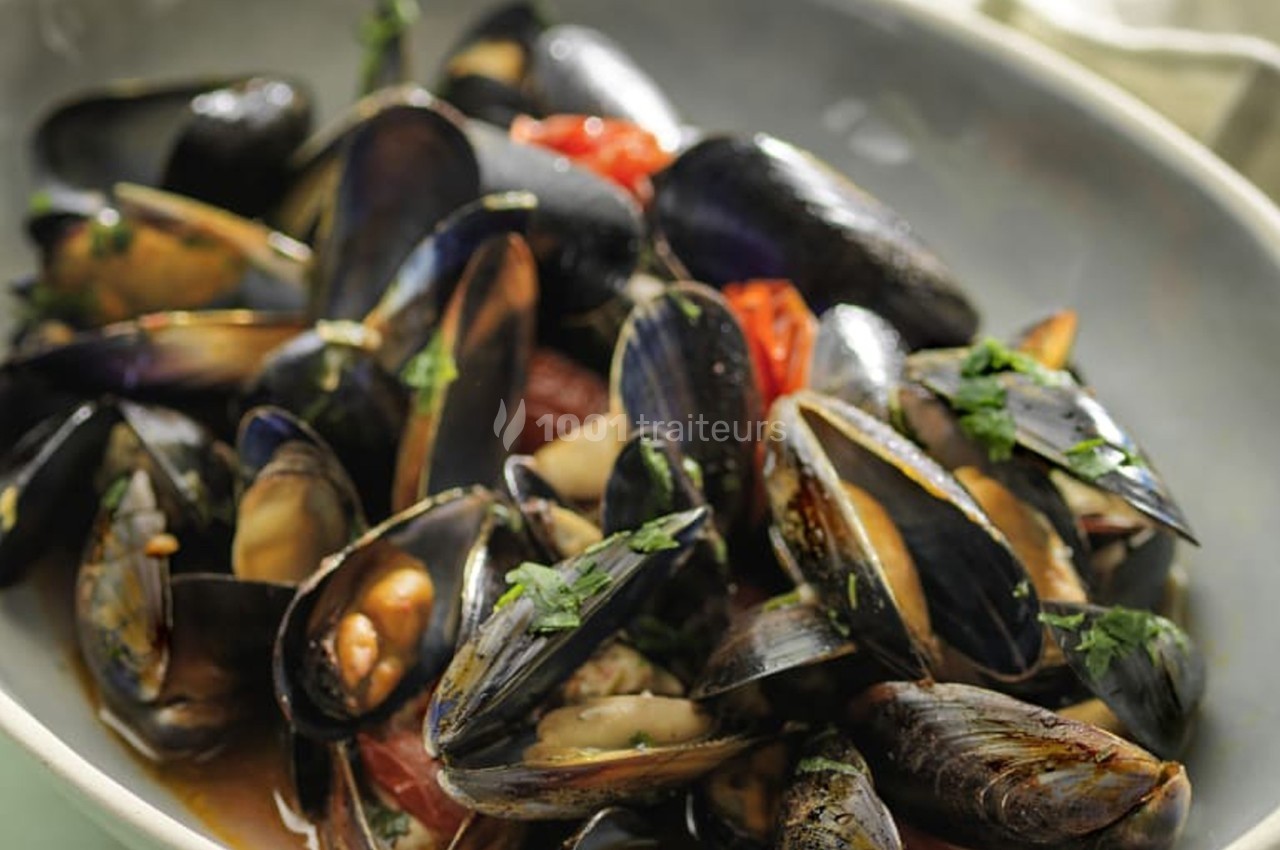 Assiette de moules cuisinées avec des tomates et des herbes fraîches, servie dans un plat ovale.