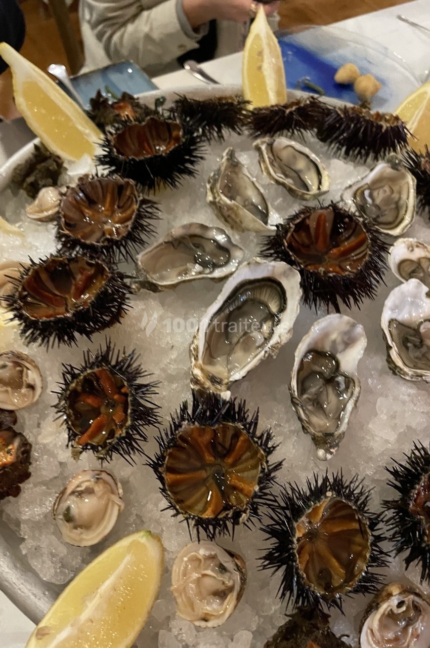 Plateau de fruits de mer avec oursins, huîtres, palourdes et quartiers de citron sur lit de glace.