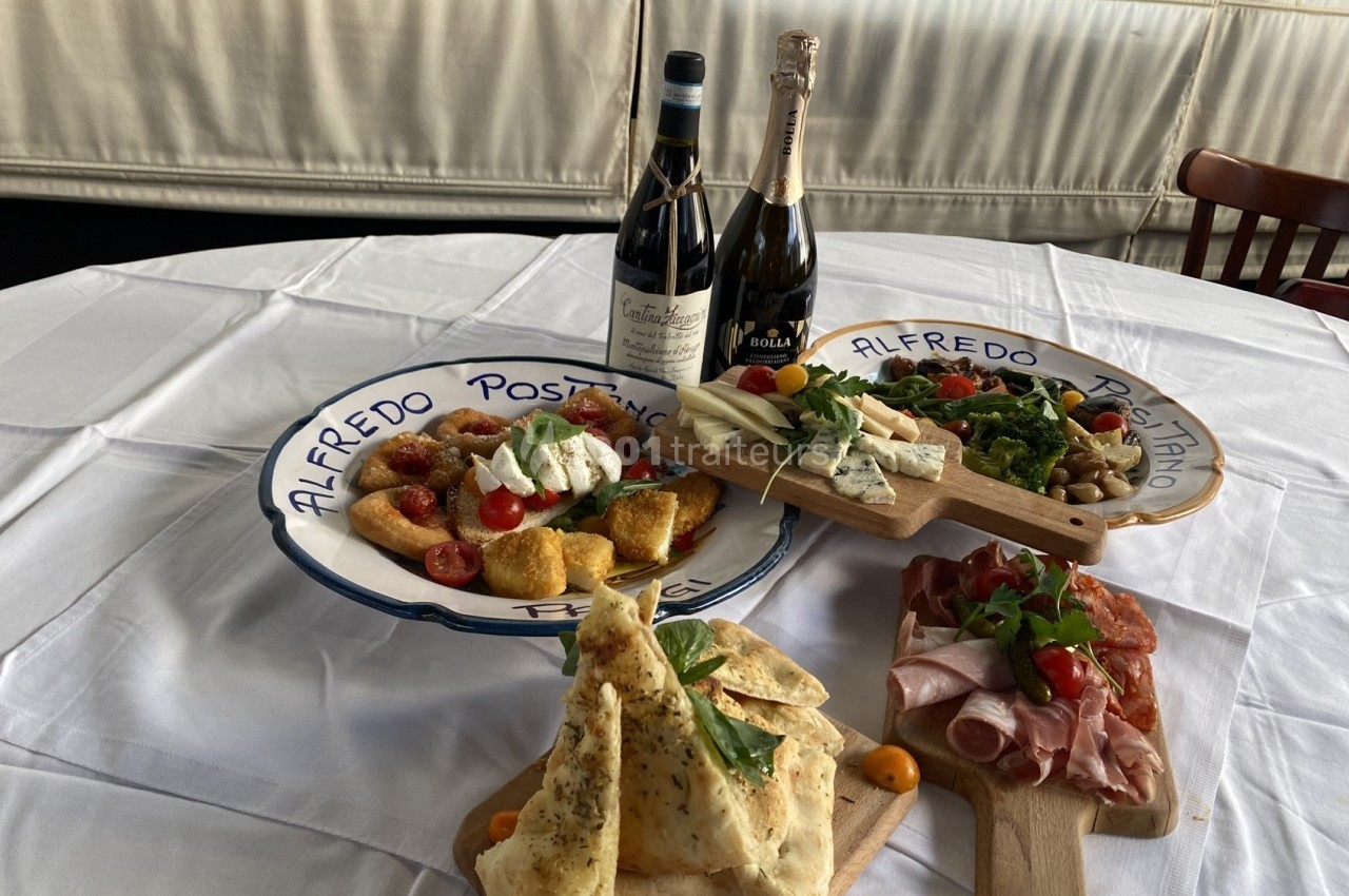 Assortiment de plats italiens avec antipasti, pain, fromages, charcuteries et deux bouteilles de vin sur une table dressée.