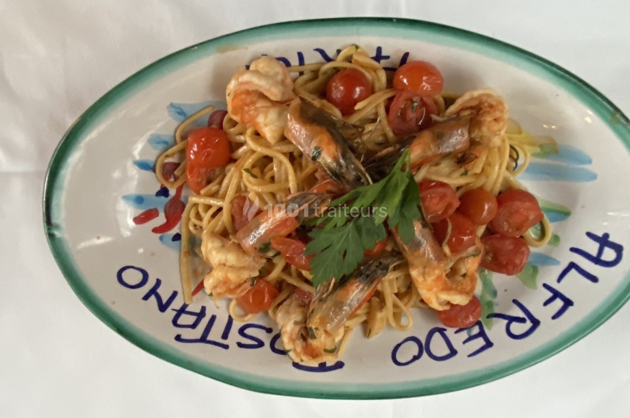 Assiette de linguines aux crevettes, tomates cerises et persil, servie sur une table avec une nappe blanche.