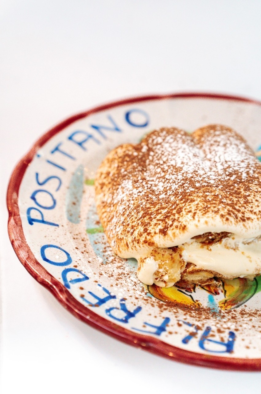 Dessert tiramisu saupoudré de cacao en poudre, présenté sur une assiette décorative avec inscription ’Positano’.