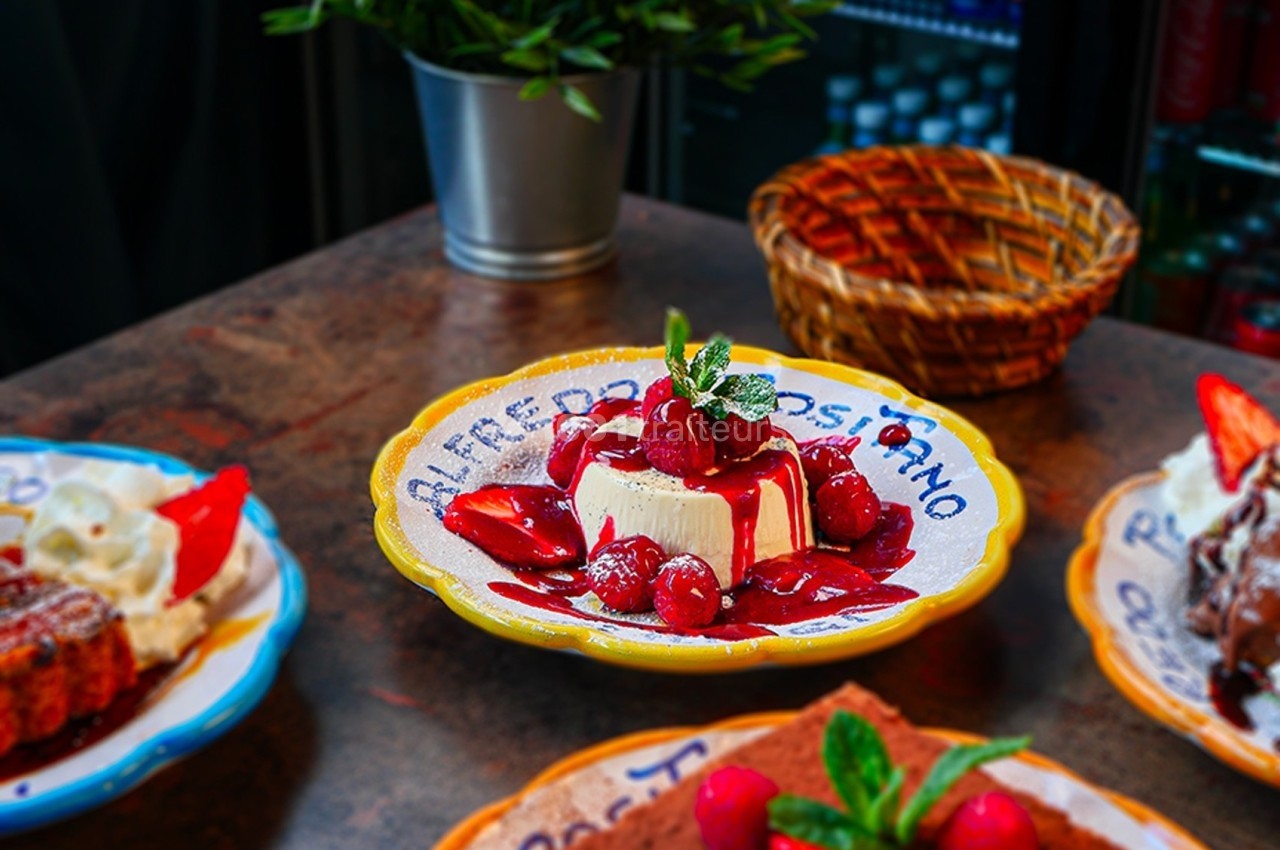 Assiette de dessert avec un cheesecake garni de fruits rouges et de menthe, posée sur une table en bois.