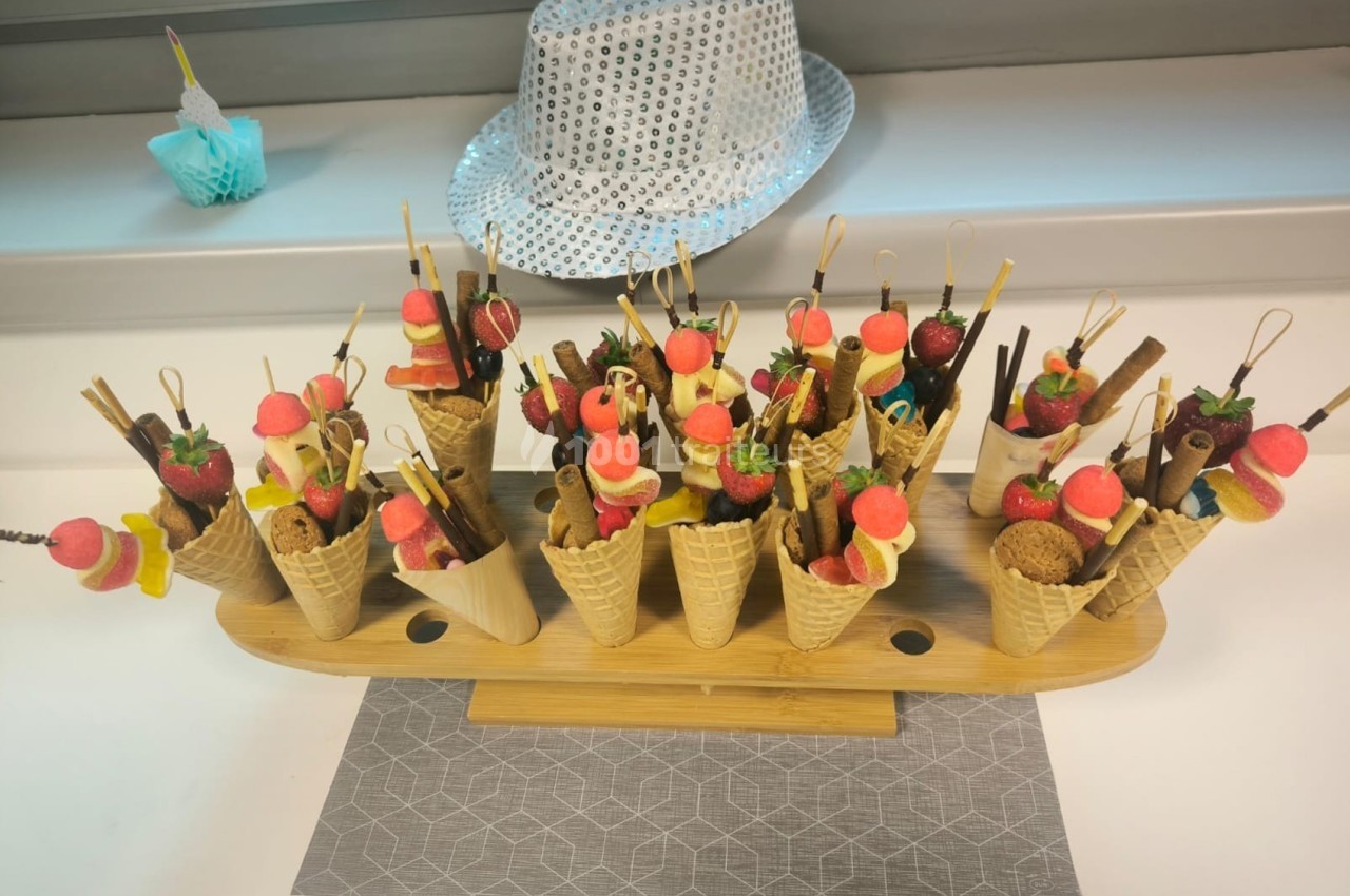Présentoir en bois avec des cornets garnis de bonbons colorés, fruits et biscuits, posé sur une table.