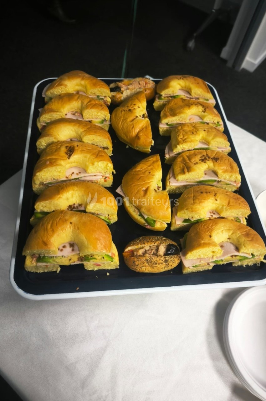 Plateau de bagels garnis de fromage, légumes et charcuterie, disposés sur une table blanche.