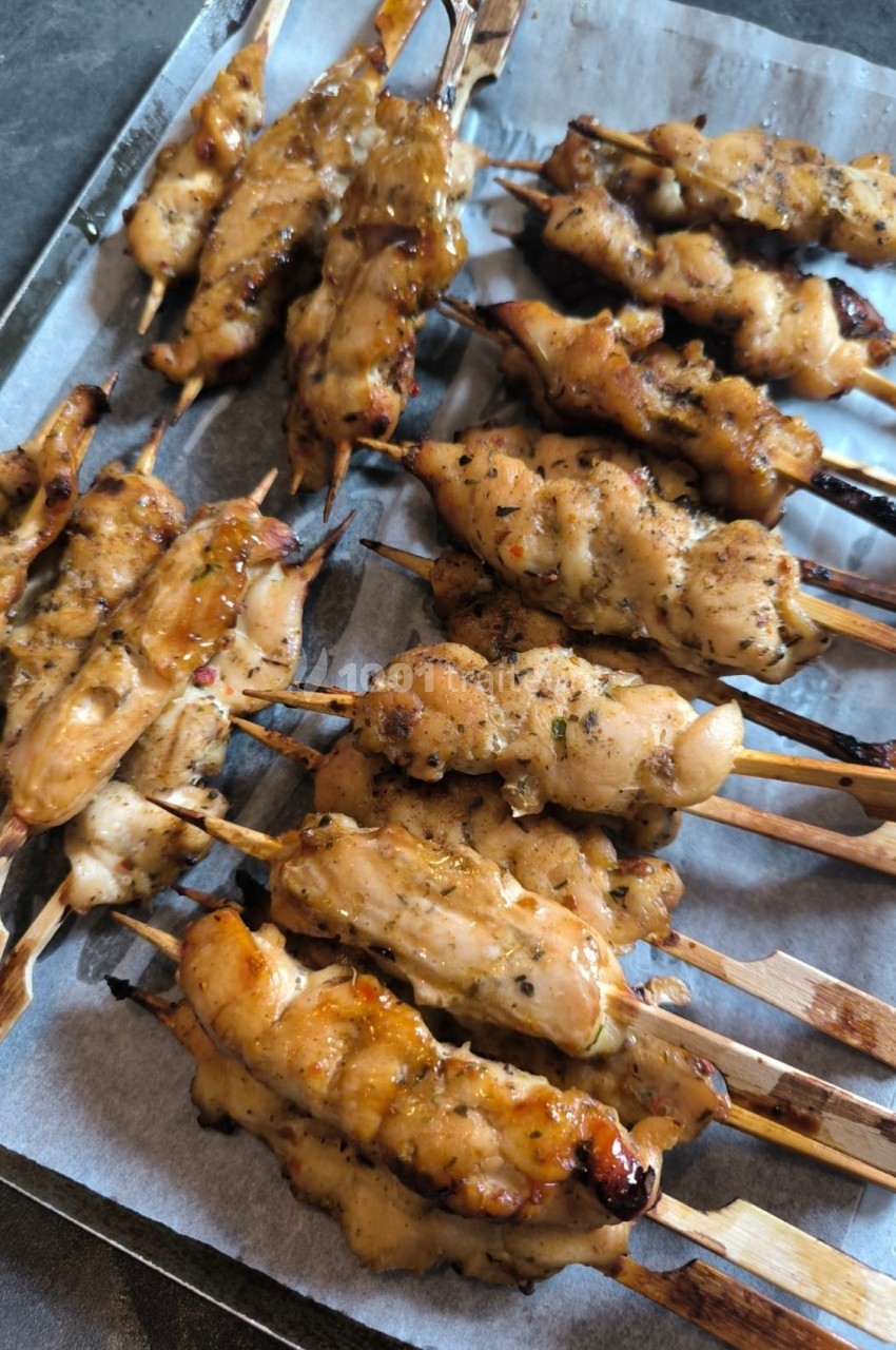 Brochettes de poulet grillées et marinées, disposées sur une plaque recouverte de papier cuisson.