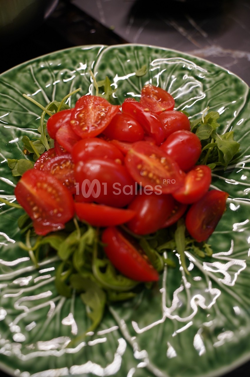 Salade de roquette garnie de tomates cerises coupées en deux, servie dans une assiette verte texturée.