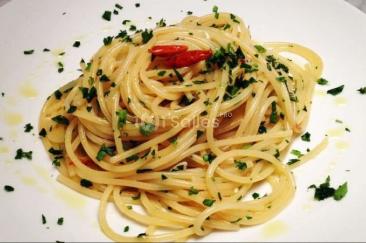 Assiette de spaghetti assaisonnés à l'huile d'olive, piment et persil, présentée sur une table blanche.