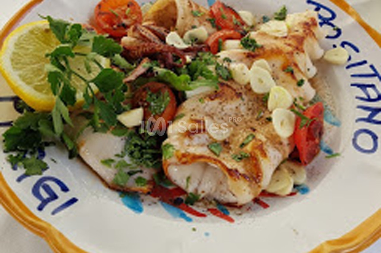 Assiette de calamars grillés garnis de tomates, ail, persil et citron, servie sur une assiette décorative.