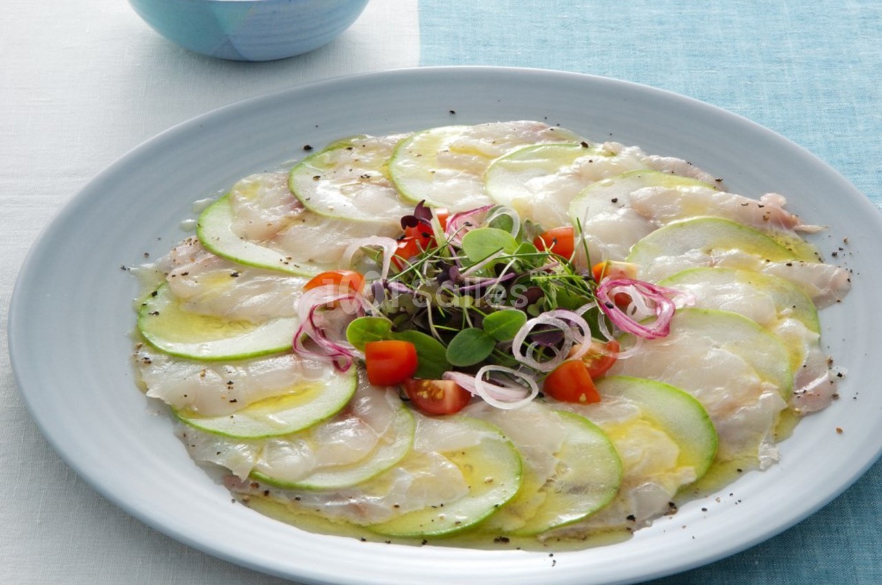Assiette de carpaccio de poisson blanc avec des tranches de courgette, tomates cerises, oignons rouges et jeunes pousses.