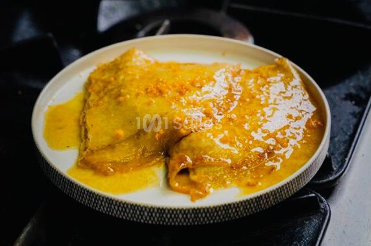 Crêpes nappées de sauce dorée servies dans une assiette ronde sur un plan de cuisson sombre.