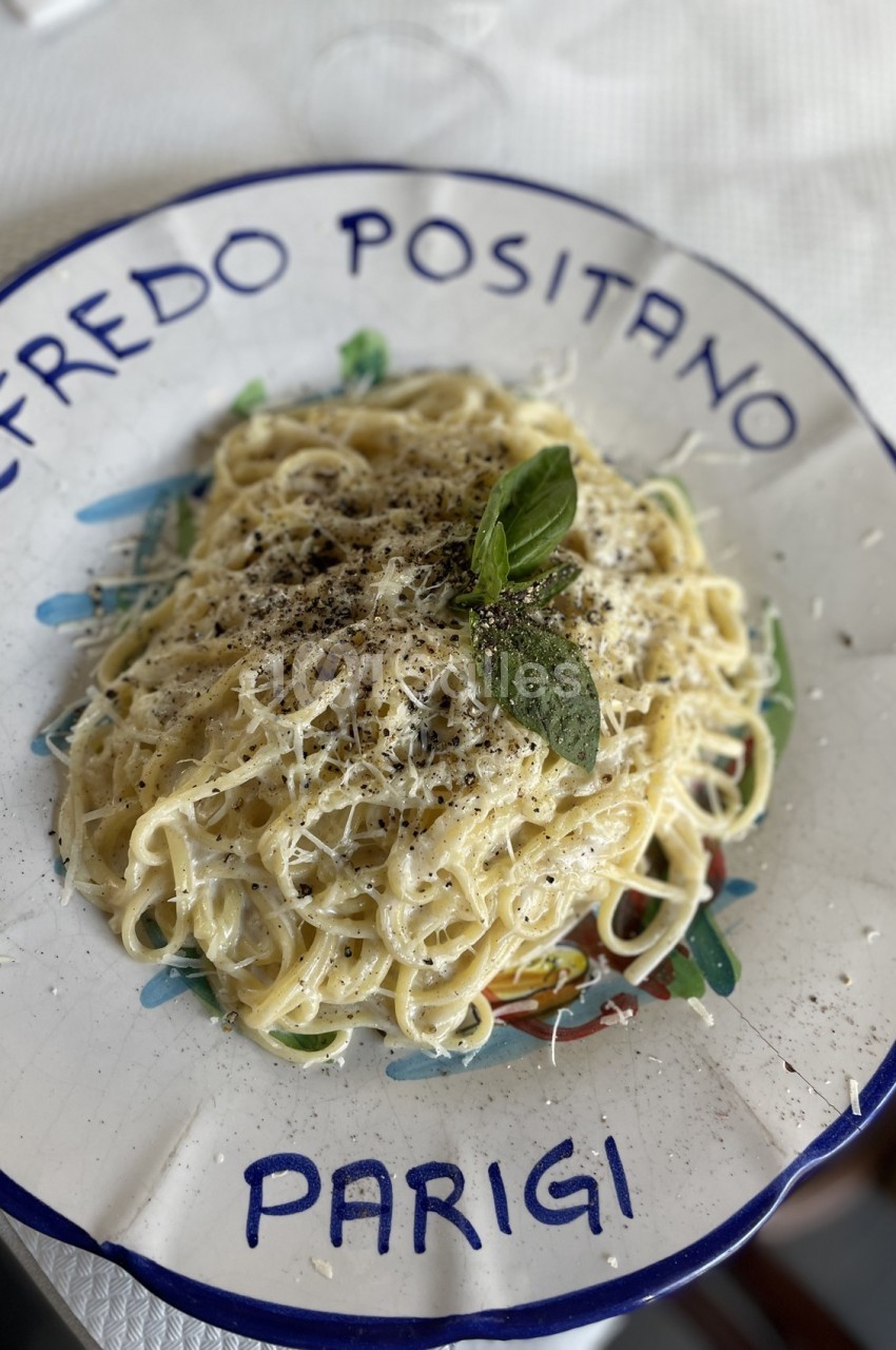 Assiette de pâtes crémeuses garnies de basilic, poivre et parmesan, servie sur une assiette décorative.